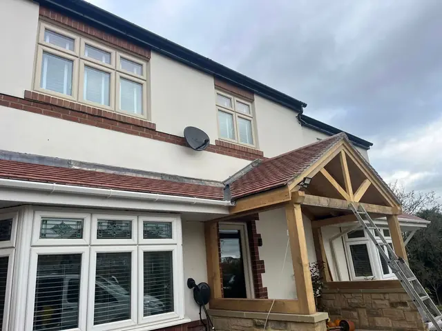Front of a rendered house with a new oak-framed porch under a red tiled roof, and a tiled canopy running along the bay window
