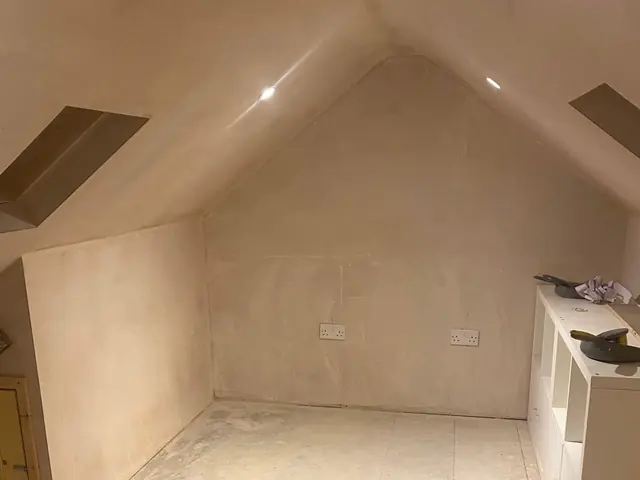 Newly plastered loft room with a roof window in each sloping ceiling, downlights and double sockets on the end wall